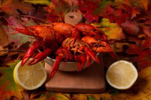 Red boiled crawfish on wooden plank with fall leaves behind it