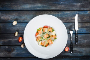 caesar salad with salmon on white plate with wooden bakground, top view